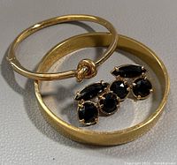 Photo of two gold-tone bracelets and pair of gold-tone black stone stud earrings on a flat surface.