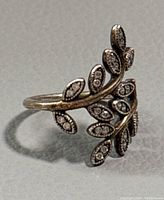 Close-up photo of silver ring with leaf design and embedded stones showing details and minor wear.