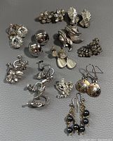 Overview image showing assortment of twelve pairs of vintage custom earrings with various styles and materials laid out on grey surface.