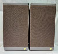 Front view of both speakers with brown fabric grilles and gray plastic cabinets