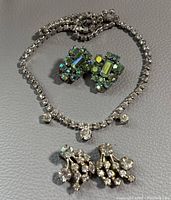 Full view of necklace with two pairs of earrings on a gray background.