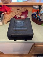 Black hard plastic carrying case labeled Jobmate, closed, placed on kitchen counter.