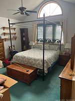 Full view of black metal 4-post queen size bed with bedding and accessories nearby in bedroom.