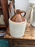 Full view of antique stoneware jug showing white base and brown glazed top with handle and spout, placed on wooden surface