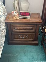 Front view of first wooden bedside table showing two drawers with metal handles and decorative inlay on top edges.