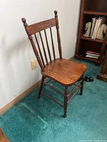 Single wooden chair with spindle backrest placed on blue-green carpet next to bookshelf.