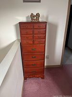 Front view of tall reddish-brown wooden chest with 12 drawers, 8 small on top, 4 large below, standing on scalloped base.