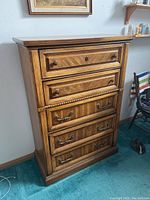 Front angle view of the wooden chest of drawers showing five drawers with two styles of handles.