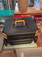 Closed black plastic carrying case labeled CMT with orange latches on each side