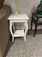 Photo showing one of the white wooden end tables with curved legs and a square top placed beside a sofa.