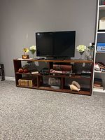 Front view of wooden entertainment stand with a television, decorative glass vases with flowers, books, and other items on shelves.
