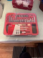 Red plastic case with variety of hobby knife blades and handles arranged in foam inserts.