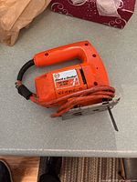 Photo of an orange Black & Decker jig saw with orange power cord on grey countertop, blade attached and label visible on the side.