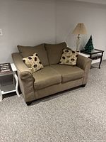 Full view of brown fabric love seat with two patterned throw pillows, located between two small white side tables with lamps and decor.