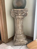 Photo of a decorative concrete pedestal column with Ionic scroll design and weathered finish.
