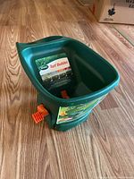 Photos show a green Scotts Turf Builder handheld seed spreader in unused condition with orange adjustment knobs and handle. Photos taken to show item condition and markings.
