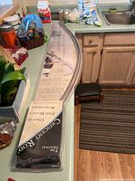 Photo of unopened boxed adjustable curved shower curtain rod and packaging on kitchen counter