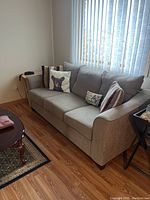 Angled side view showing the sofa placed near window with curtains and side tables around it.