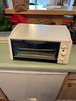 Front view of white Oster toaster oven showing glass door and control dials.