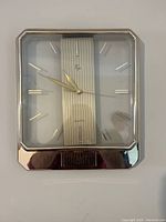 Front view of vintage 1980s square quartz wall clock with chrome-tone frame, striped clock face, and gold-tone hands and markers.