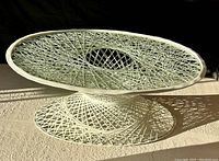 Oval woven spun fiberglass coffee table in white with glass top, photographed under natural light showing detailed woven pattern and table shape.