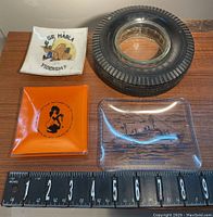 All four vintage glass ashtrays shown together with measuring scale to display size and detail of text and design.