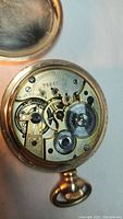 Close-up of the pocket watch movement showing gears and 15 jewels marking, indicating the mechanical inner workings of the watch.