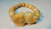 Close-up of carved animal figure bead and yellow round beads showing polished surface on bracelet.