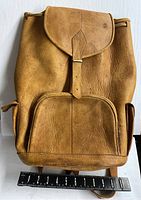 Front view of the natural leather backpack showing flap closure, front pocket, and side pockets with ruler for scale