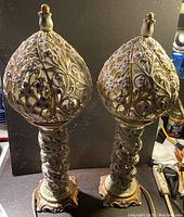 Front view of both ornate ceramic lamps, showing detailed floral and vine design with small bird finials on top.