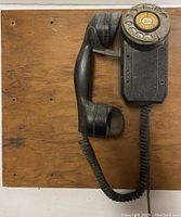 Front view of vintage rotary dial phone mounted on wooden board showing handset and base.
