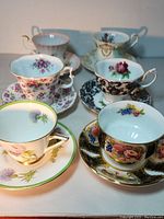 Full set of six fine china cups and saucers arranged in two rows showing floral and gold trim details.