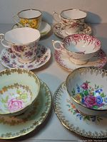 Photo showing all six fine china cups and matching saucers with different floral patterns and gold trim.