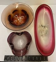 Top view of three glass bowls including oblong bowl with red rim, smokey round bowl, and purple bowl with diamond base