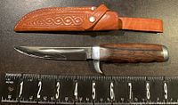 Fixed blade hunting knife with clip point blade and wood handle shown with measuring tape for size reference
