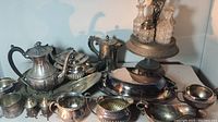 Overview photo showing assorted silverplate items including teapots, sugar bowl, salt and pepper shakers, and glass decanters on pedestal stand.