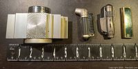 All four lighters lined up next to a ruler showing size comparison. Includes the large sixties style table lighter, two military style lighters, and the slender Coca-Cola lighter.