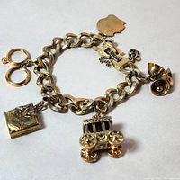 Vintage gold tone Monet charm bracelet displayed with all charms visible: book, carriage, bells, padlock, and face silhouette.