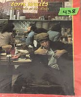Front cover of Tom Waits 'Nighthawks at the Diner' showing the album artwork with Waits in a diner setting.