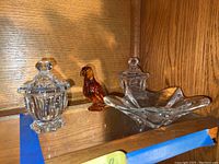 Group shot showing two covered crystal bowls with lids, a star-shaped dish, and amber bird figurine