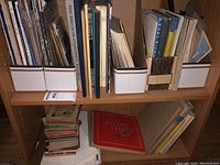 Shelf with multiple Olympic bulletins and reference books in white archival boxes