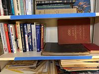 Shelf containing several books related to Olympic history and other vintage subjects, visible titles include 'The Olympic Marathon', 'Boycott', and 'The Nazi Olympic Challenge'.