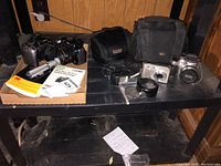 Lot contents showing Canon, Kodak, HP Cameras, tripod, two black camera cases, and empty cases on black table.