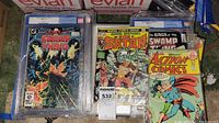 Three CGC slabbed comics on floor: two Saga of the Swamp Thing issues and one Marvel Spotlight: The Son of Satan