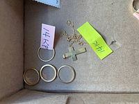 All four rings, gold cross pendant, and chain arranged in box