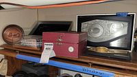 Full view of lot on wooden shelf: round plaque, two metal plaques, glass boat box, stadium model under cover