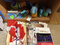 Top shelf showing plush, inflatable and packaged dog toys with stacks of Olympic and sports ephemera below