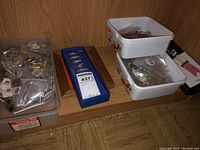 Shelf with large plastic bin of loose bagged pins, two white plastic containers of pins, blue box and wooden frame rails