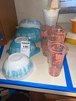 Three turquoise and white Pyrex Butterprint mixing bowls and five pink elephant glasses.