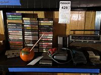 Shelf with stacks of cassette tapes, an orange novelty cup, Sony Walkman, deteriorating red foam headphones, and Panasonic FM-AM 2-band receiver